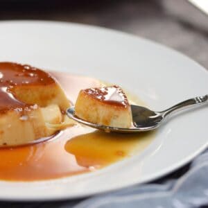 creamy caramel flan with a spoonful pulled out and resting on a white plate.