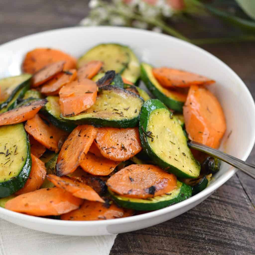 angle cut carrots and zucchini that have been sauteed and placed in a white bowl.