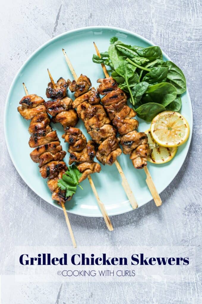 Cooked chicken thighs on bamboo skewers with salad and lemon on the side. 