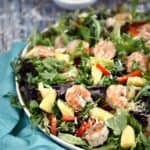 Grilled Shrimp on a mixed greens salad tossed with Pina Colada Vinaigrette, pineapple chunks, and shredded coconut on a large white platter.