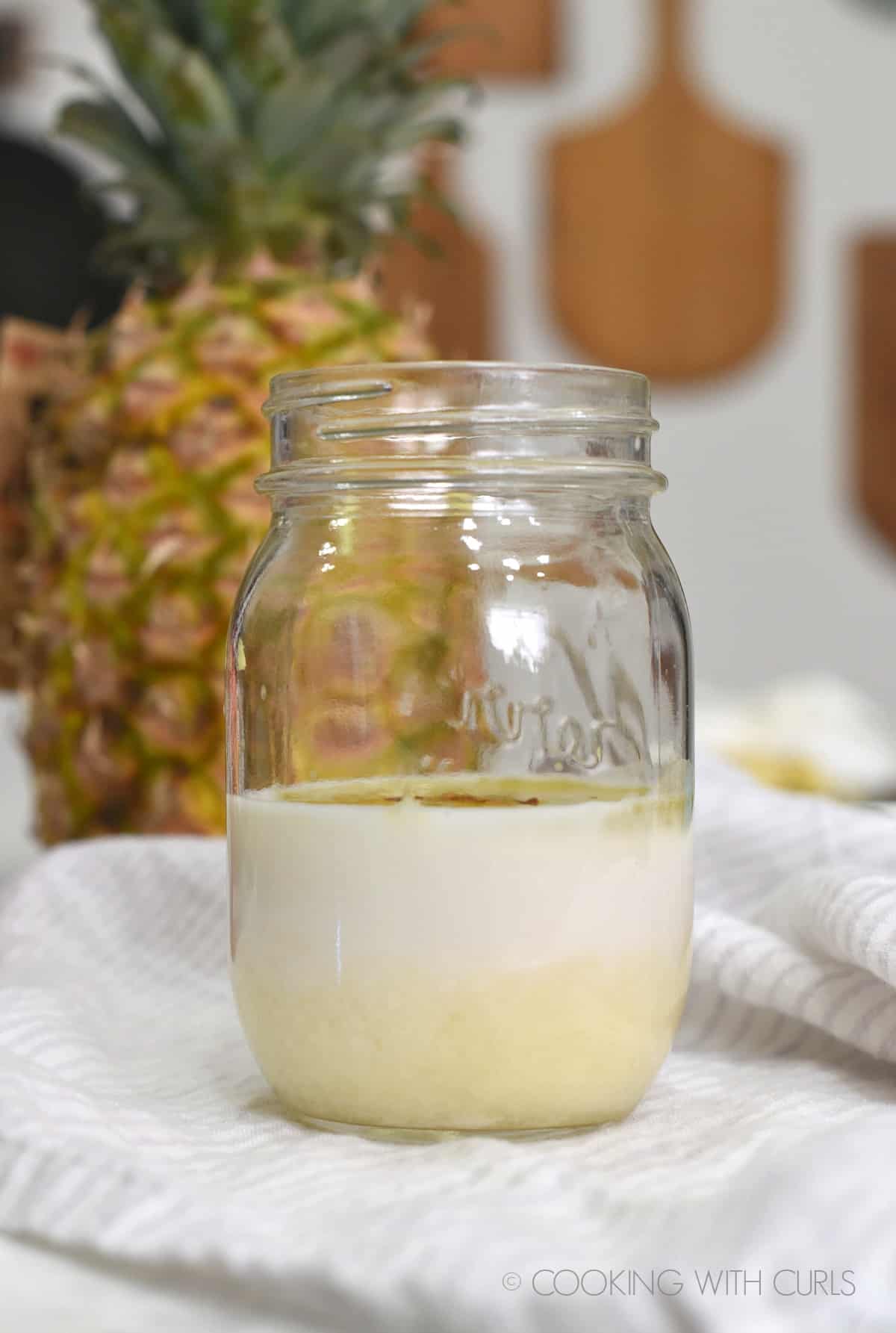 Pina Colada Vinaigrette in a glass mason jar sitting in front of a fresh pineapple. 