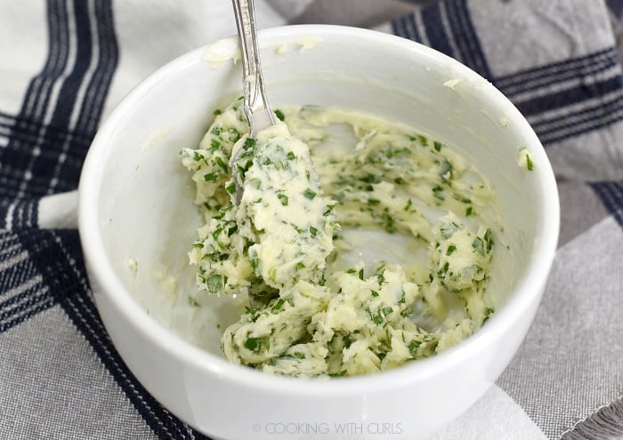 Softened butter, parsley, garlic and lemon juice mixed together with a fork in a small white bowl. 