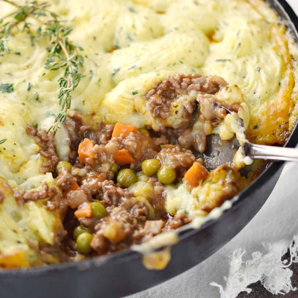 a close-up look at shepherd's pie in a skillet with a big scoop taken out of the lower right corner.
