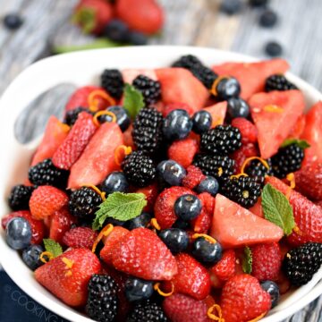 Watermelon, blackberries, blueberries and strawberries fruit salad tossed together in a large white serving bowl and garnished with mint leaves.