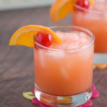 A small glass of Caribbean Rum Punch garnished with a cherry and orange wheel with a second cocktail in the background.