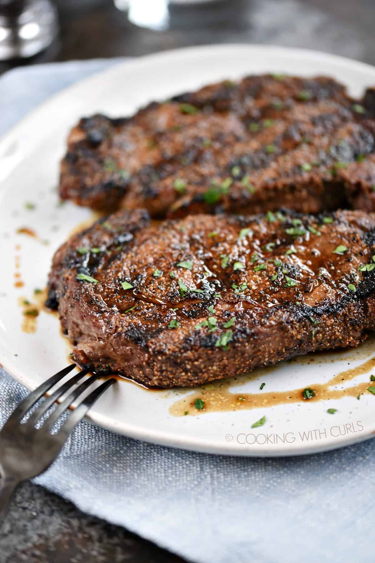 Two Perfect Grilled Ribeye Steaks resting on a plate. 