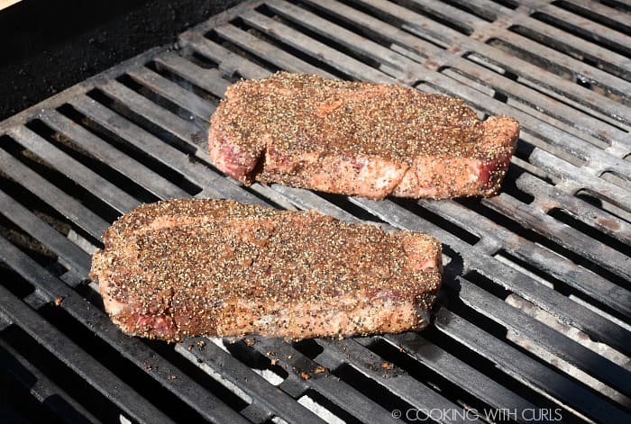 Two seasoned steaks on a hot grill. 