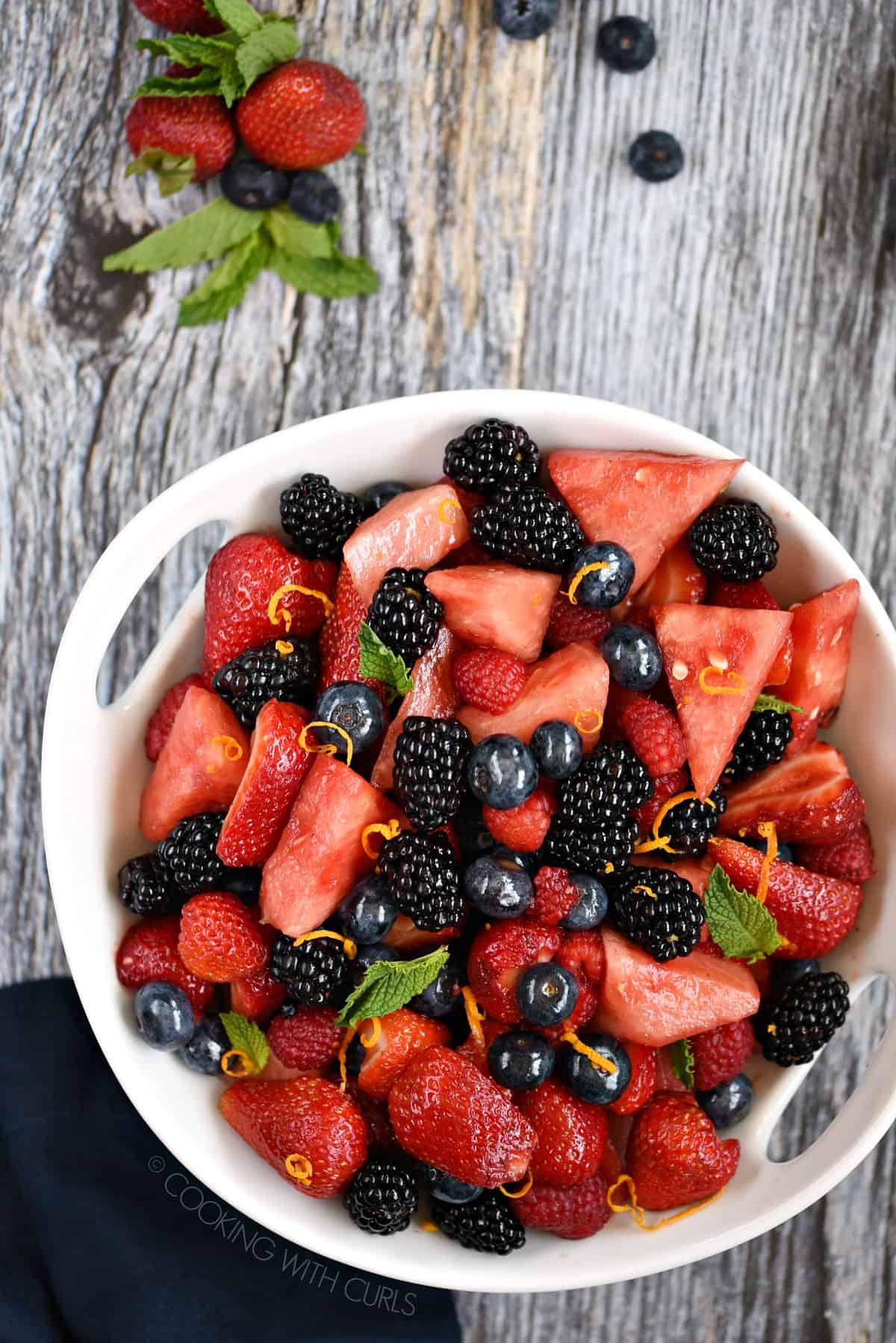 Looking down on watermelon, blackberries, raspberries, strawberries and blueberries tossed together in a large white serving bowl.