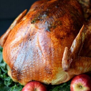 close-up of a whole roasted turkey sitting on a bed of greens with whole apples around the bottom.