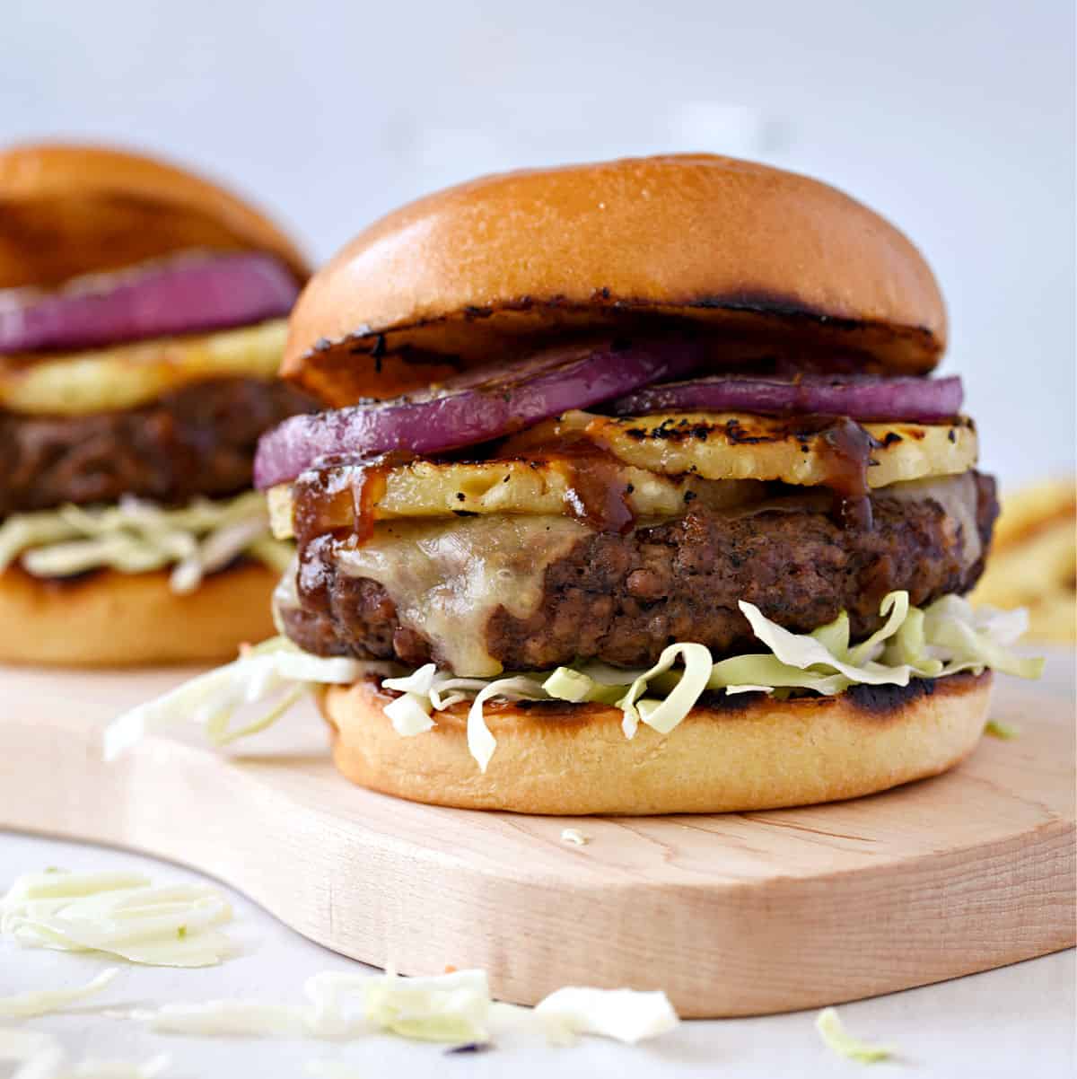 Two Grilled Hawaiian Teriyaki Burgers topped with grilled pineapple, onions, shredded cabbage on brioche bun.