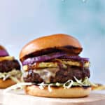 Two Grilled Hawaiian Teriyaki Burgers topped with grilled pineapple, onions, shredded cabbage on brioche bun.