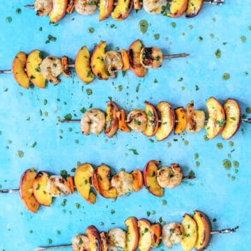 looking down on grilled shrimp and peach skewers drizzled with glaze on a blue background.