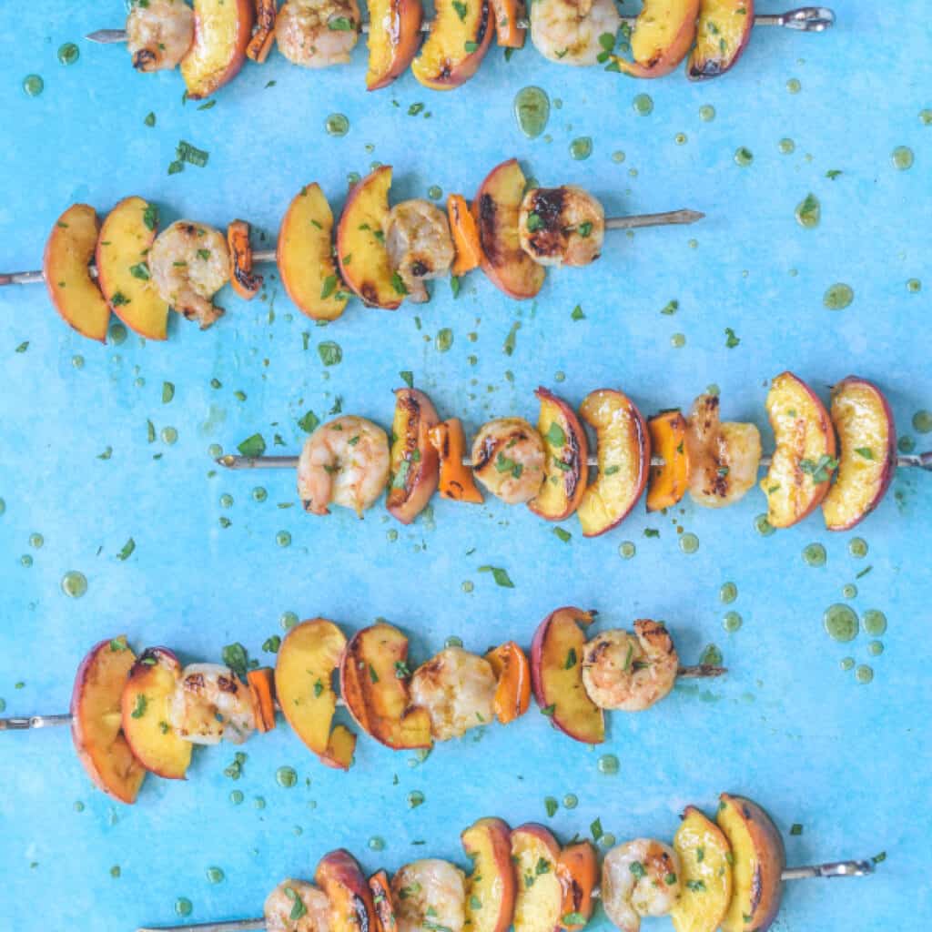 looking down on grilled shrimp and peach skewers drizzled with glaze on a blue background.