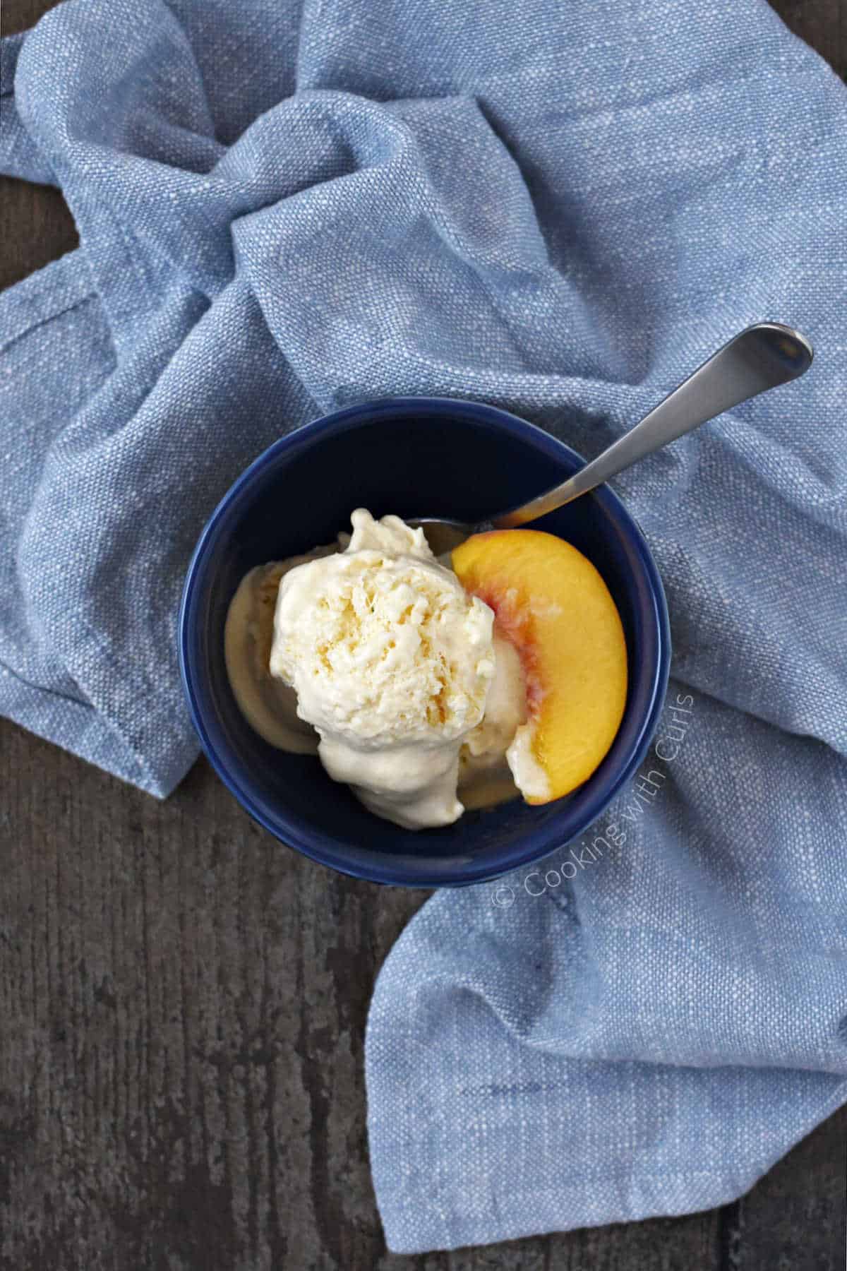 Looking down on a bowl of peach ice cream with a peach slice and spoon on the side.