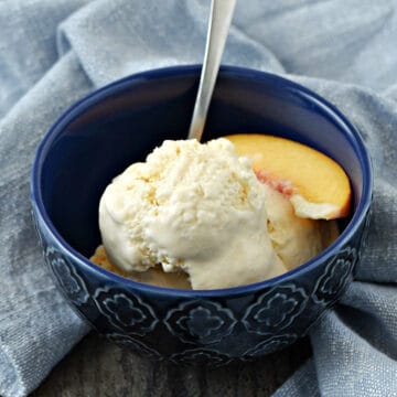 A bowl of peach ice cream with a peach slice and spoon.