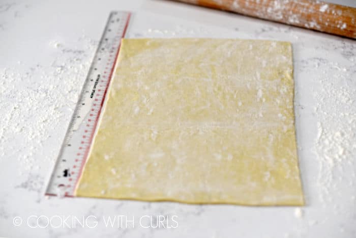 Puff pastry on a floured work surface with a ruler to the left and a rolling pin across the right corner. 