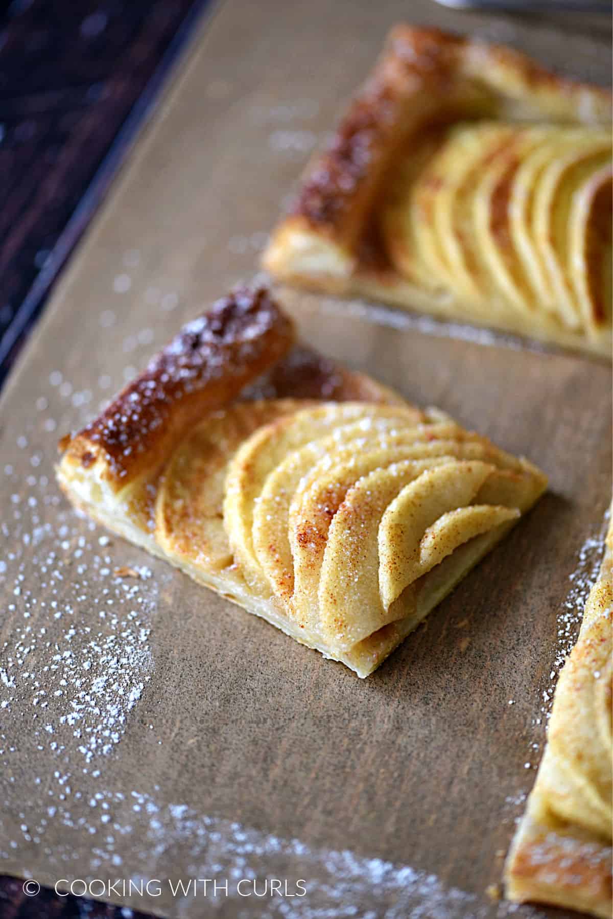 a slice of puff pastry apple tart at an angle on parchment paper dusted with powdered sugar.