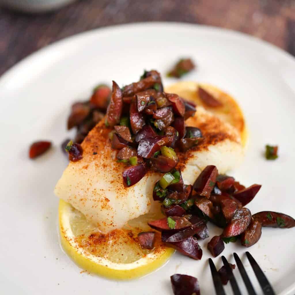 baked cod topped with cherry salsa sitting on two lemon slices on a white plate.