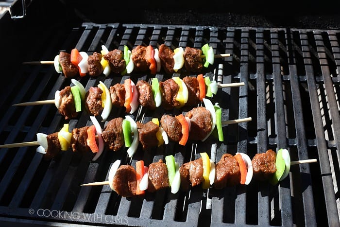 four wooden skewers threaded with steak cubes, onions and bell peppers on a hot grill. 