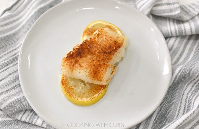 seasoned baked cod filet on two lemon slices sitting on a white plate.