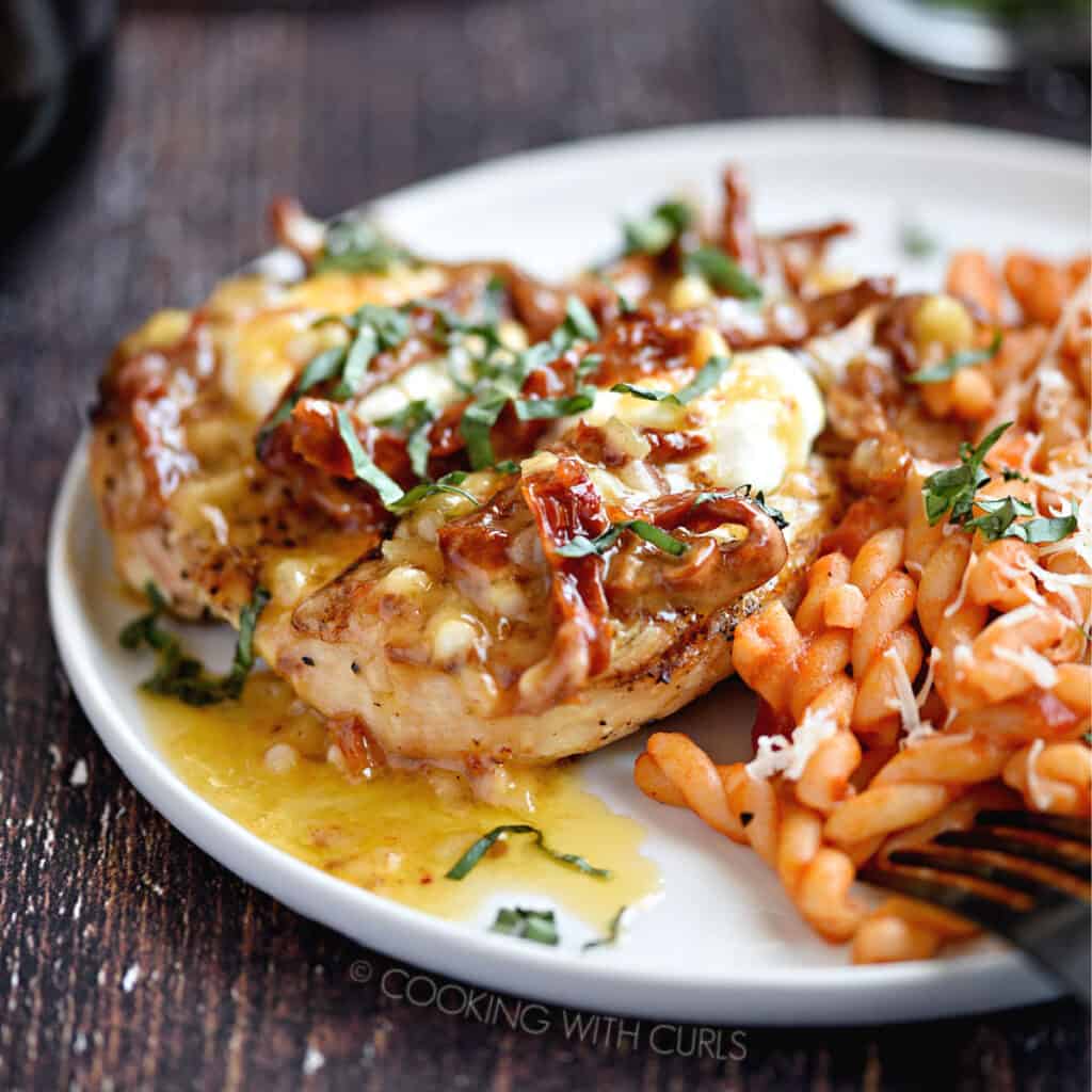 a close-up image of Chicken Bryan with a side of pasta on a white plate.