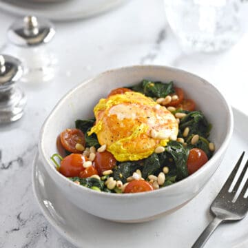 a turmeric poached egg split open over a bed of sauteed spinach and cherry tomato halves sprinkled with toasted pine nuts.
