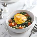 a bright yellow poached egg on a bed of sauteed spinach and cherry tomato halves sprinkled with toasted pine nuts.