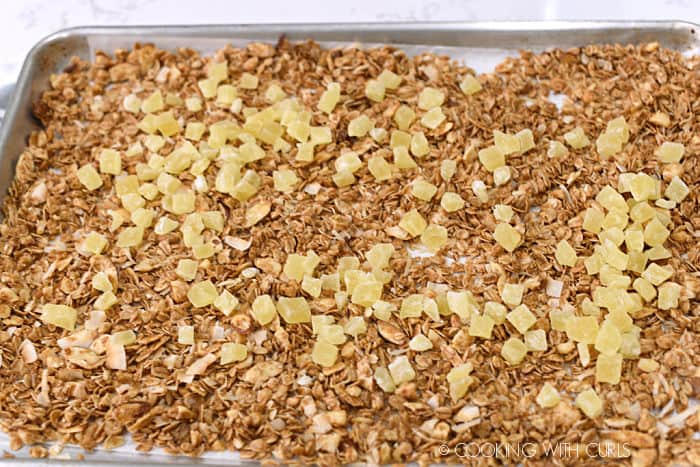 dried pineapple chunks added to the pina colada granola in a rimmed baking sheet. 