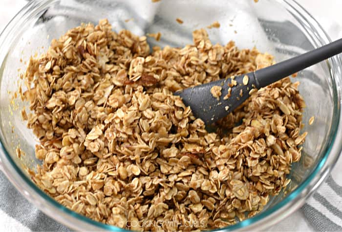 oat and nut mixture mixed together with the coconut oil, agave syrup and flavoring in a large glass bowl with a gray rubber spatula. 