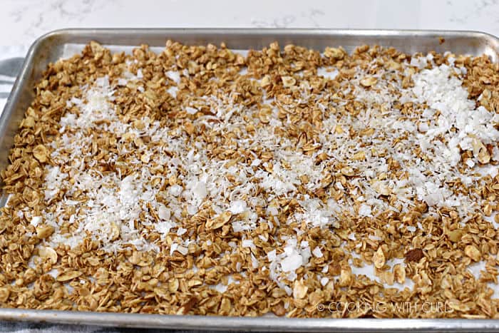 shredded and shaved coconut added to the pina colada granola on a baking sheet. 