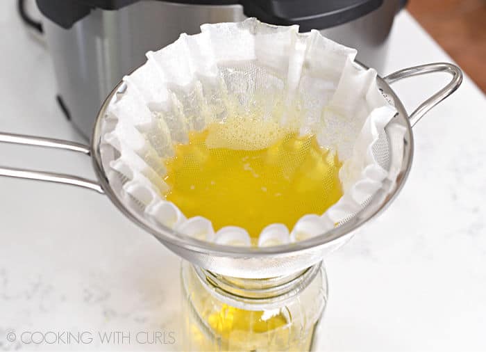 Clarified butter poured into a glass jar through a coffee filter lined metal strainer. 