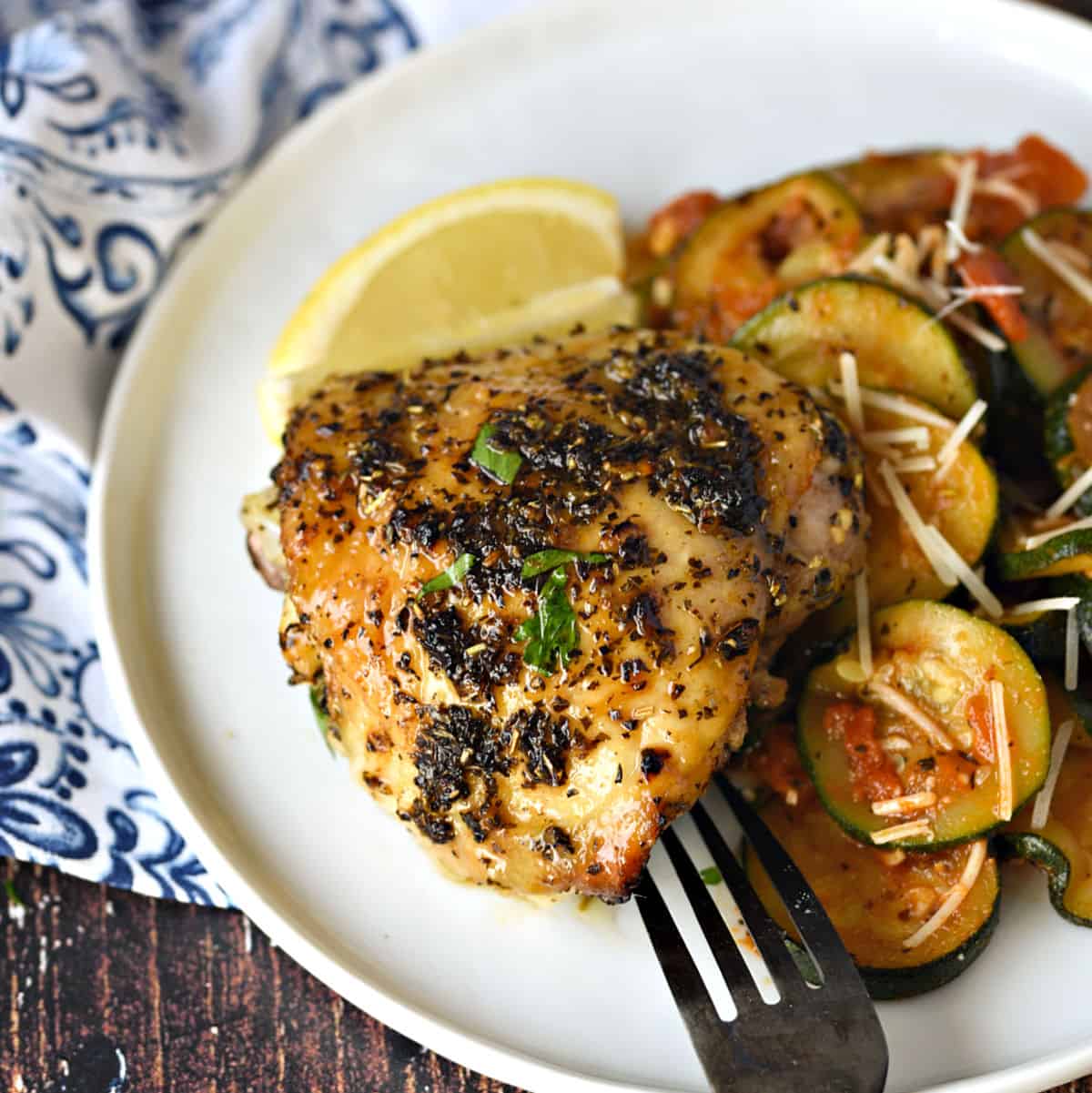 Crispy and delicious Italian Baked Chicken Thighs on a white plate with sautéed zucchini and tomatoes.