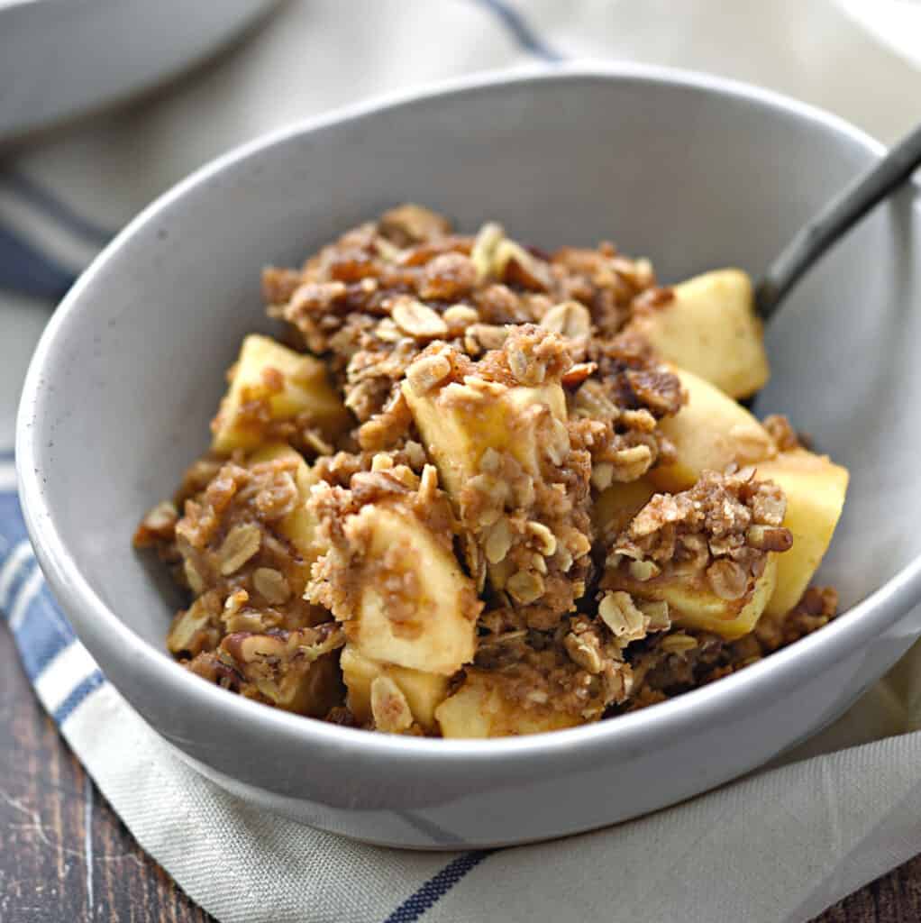 Instant Pot Apple Crisp in a white bowl with a black spoon leaning against the edge.