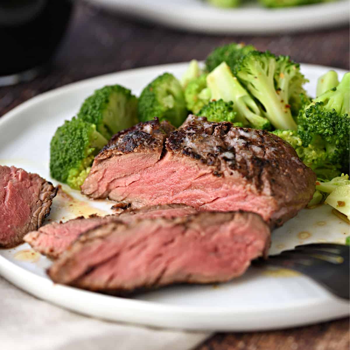 Perfectly cooked Sous Vide Filet Mignon in an Instant Pot sliced on a white plate with broccoli florets on the backside.