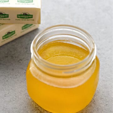 a one pint jar filled with melted ghee with two sticks of butter in the background.