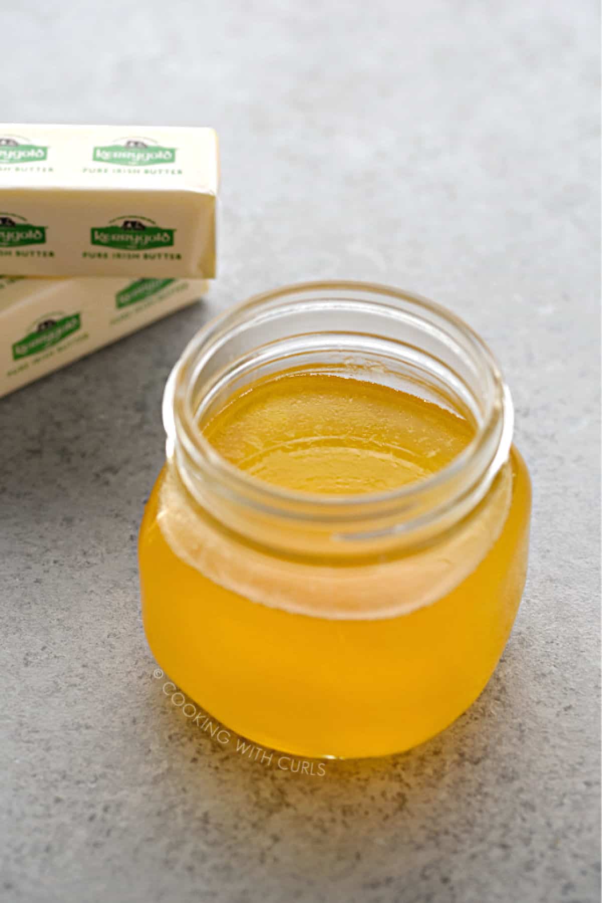 looking into the top of a glass jar filled with melted ghee, with two sticks of butter in the background.