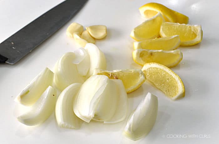 lemon and onion wedges on a white cutting board with a chefs knife on the left hand side. 