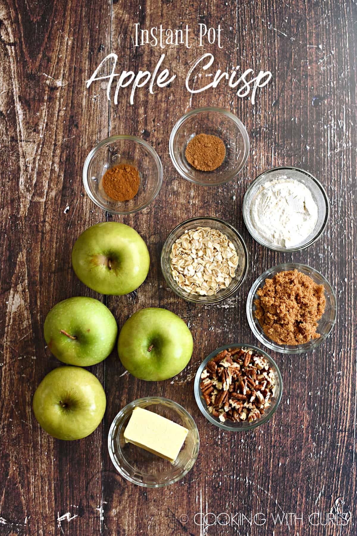 looking down on four green apples and glass bowls filled with cinnamon, nutmeg, flour, oats, brown sugar, pecans and butter. 
