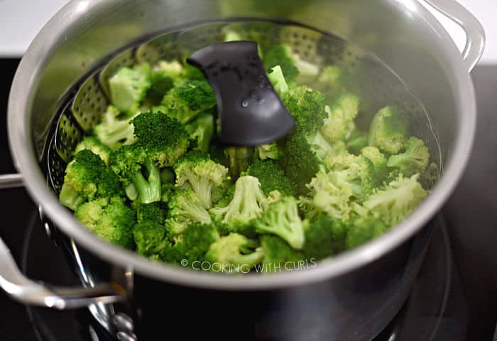 steamed broccoli in a steamer basket inside a large pot sitting on the stove. 