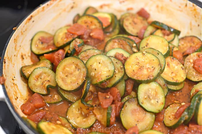 zucchini slices and diced tomatoes cooked until liquid is absorbed in a large white skillet.