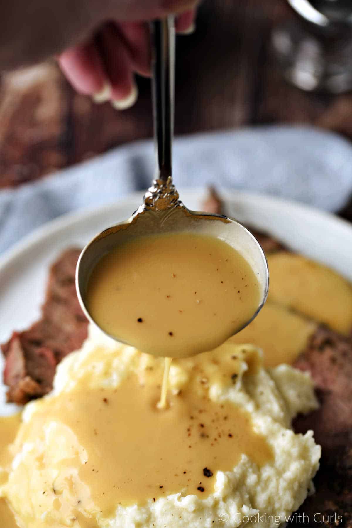 Beef gravy being poured onto mashed cauliflower and slices of roast beef from a silver ladle.