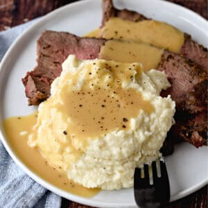 a close-up image of sliced roast beef and mashed cauliflower on a plate, topped with beef gravy and black pepper.