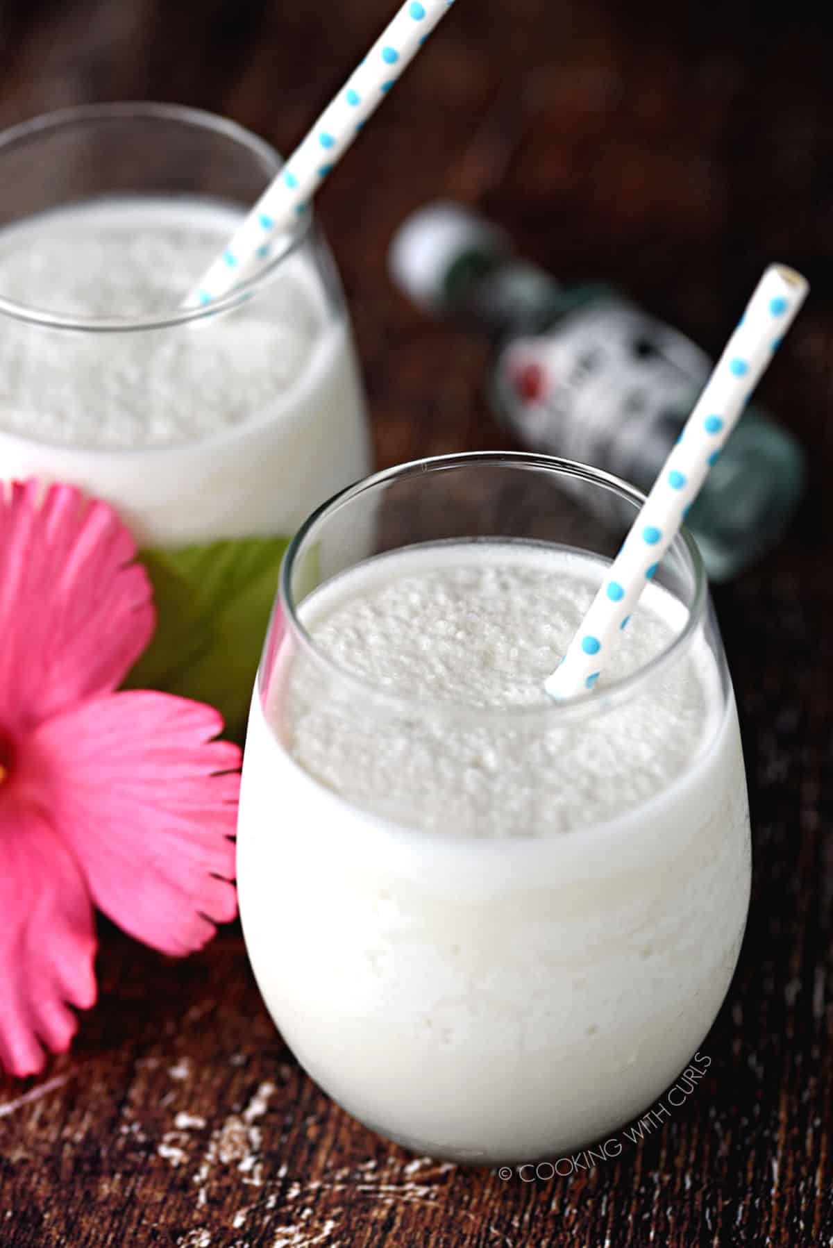 two glasses filled with thick and creamy keto pina colada cocktails with a pink flower between the glasses.