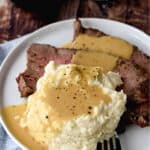a small white plate topped with slices of roast beef, mashed cauliflower and beef gravy.