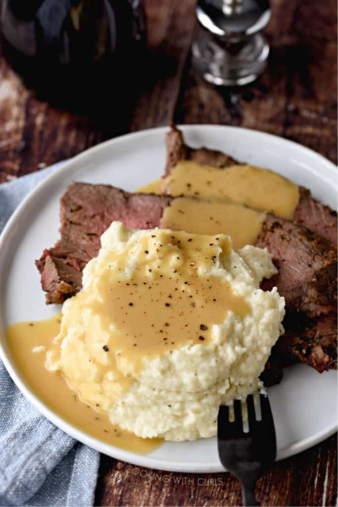 a small white plate topped with slices of roast beef, mashed cauliflower and beef gravy.