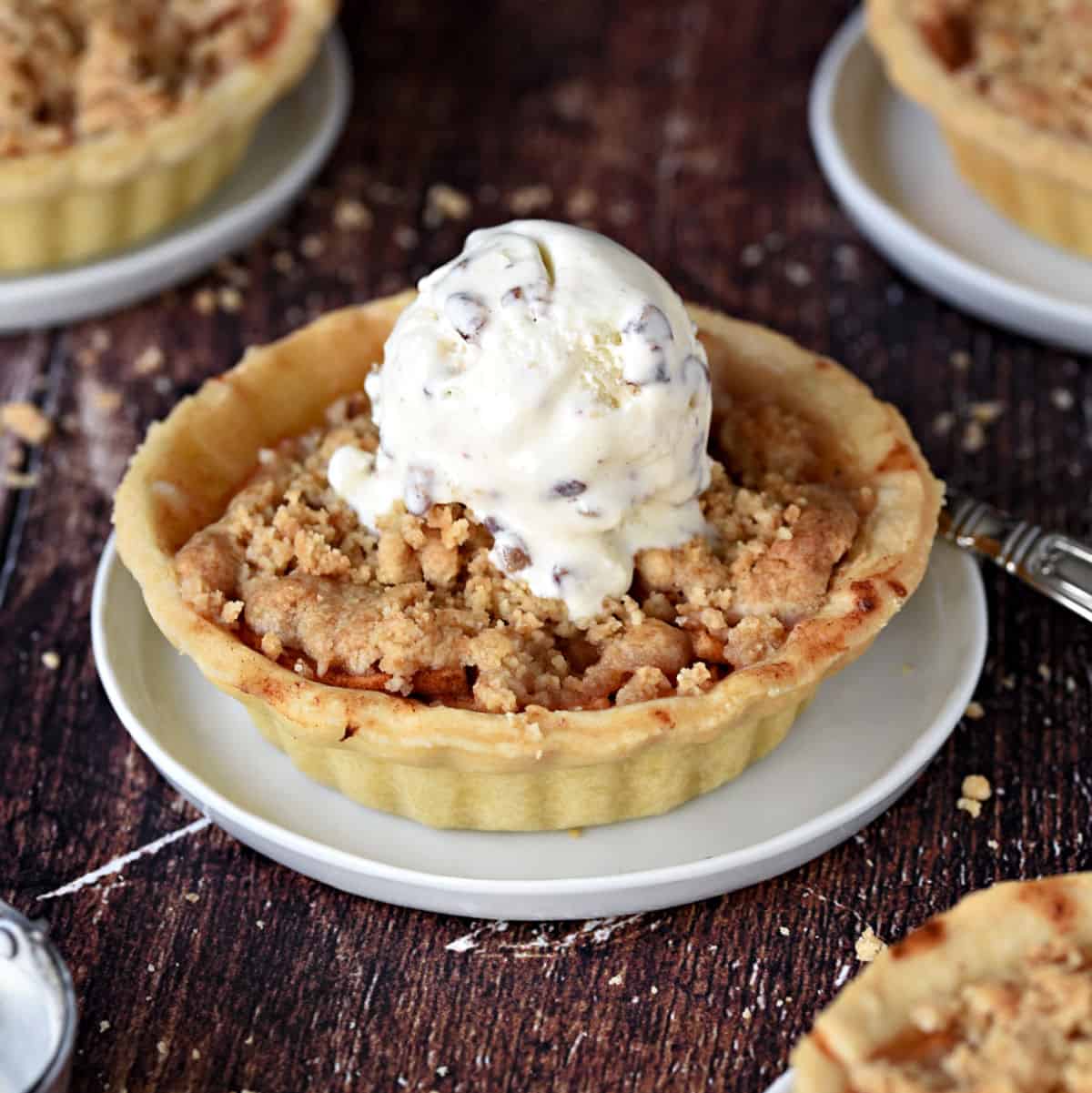 A Mini Dutch Apple Pie topped with ice cream surrounded by three other mini pies. cookingwithcurls.com