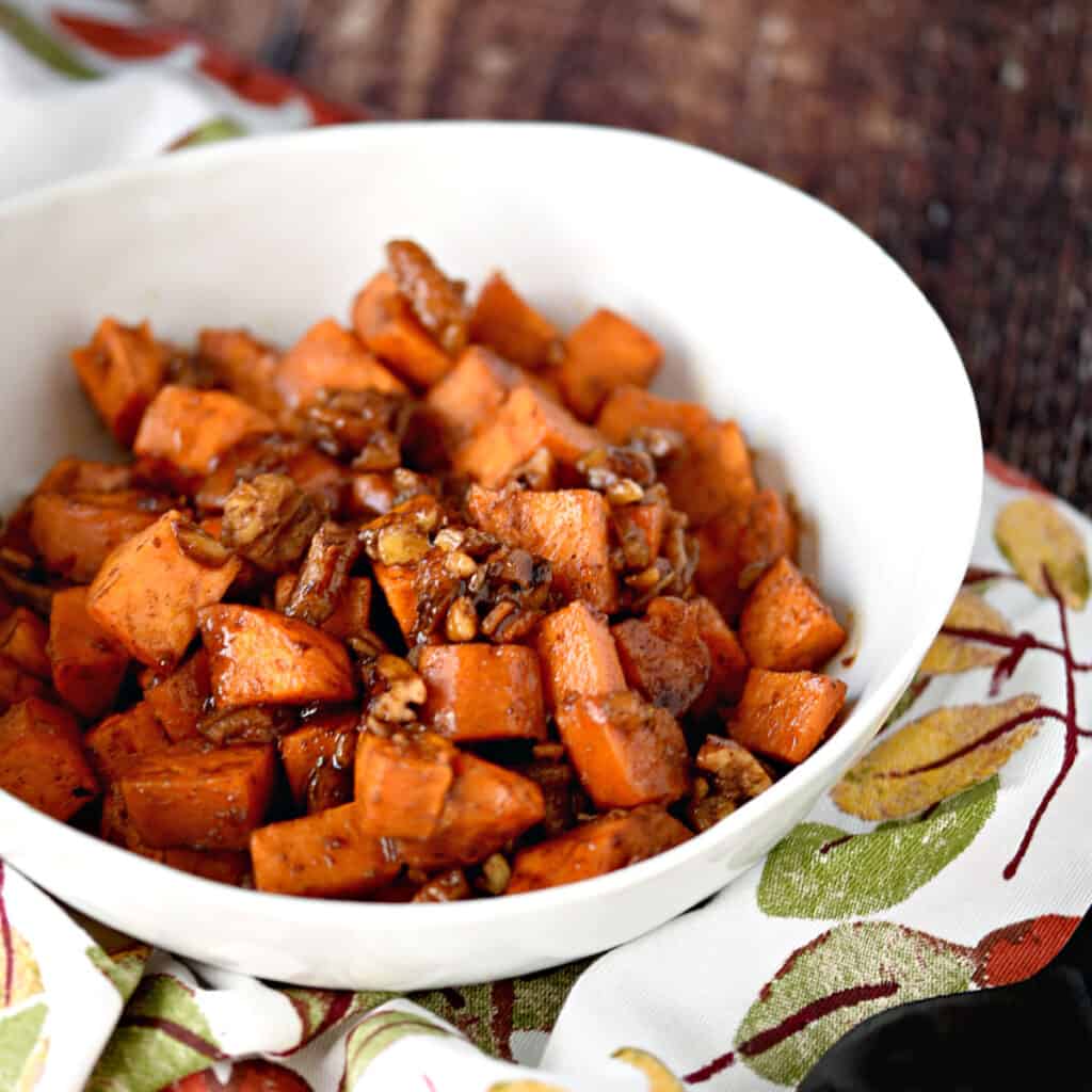 a white bowl with yam cubes and pecans sitting on a napkin with fall leaves.