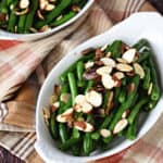 two white au gratin dishes sitting on a fall plaid napkin with green beans, shallots and sliced almonds on top.