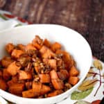 sweet potato cubes with pecans in a white bowl, sitting on a napkin with fall colored leaves.