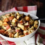 a white bowl filled with sausage, apple and cranberry stuffing sitting on a red plaid napkin.